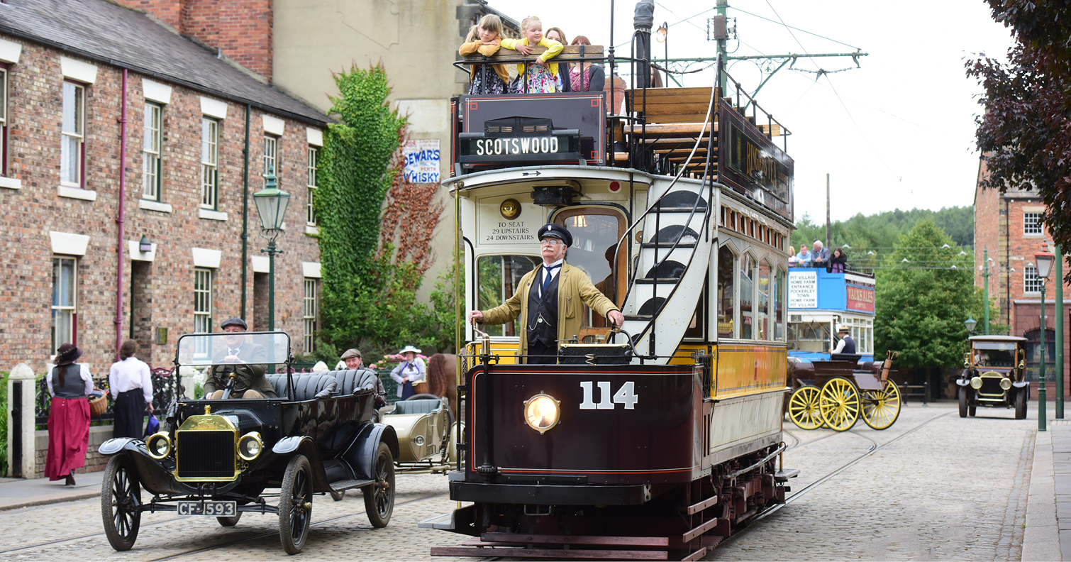 view of people riding historic tram and cars at Beamish Museum